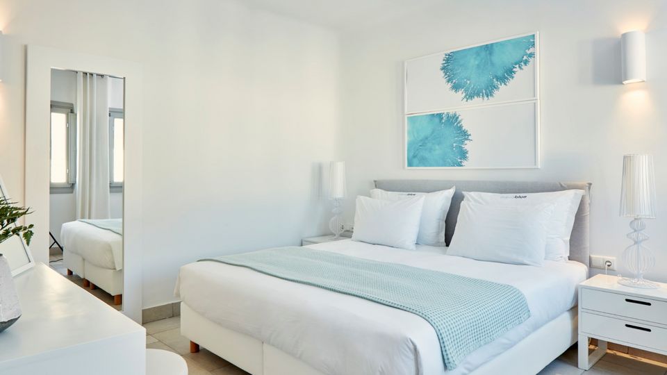 Helles, modern eingerichtetes Doppelzimmer in Weiß- und Blautönen mit gemütlichem Bett, stilvollen Dekoelementen und ruhiger Wohlfühlatmosphäre.