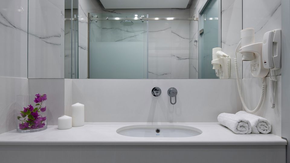 Modernes Badezimmer in elegantem Marmor-Design mit großer Dusche, breitem Spiegel und stilvollen Details – ideal für entspannte Wohlfühlmomente während des Urlaubs.