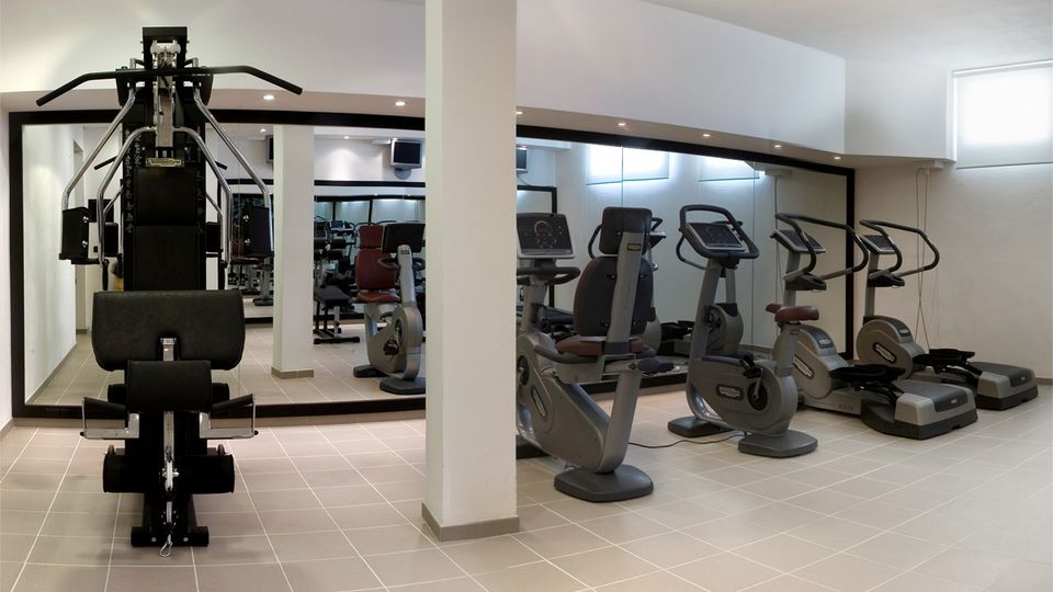 Heller Fitnessraum mit modernen Cardiogeräten, Kraftstation und großen Spiegeln – ideal für sportlich aktive Urlaubsgäste.