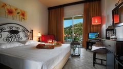 Gemütliches Hotelzimmer mit romantischem Flair, einem großen Doppelbett mit dekorativem Schmiedeeisen-Kopfteil, warmen Farbtönen, stilvollen Lampen und Zugang zum Balkon mit Blick ins Grüne.
