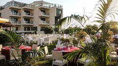 Stilvoll gedeckte Tische auf einer gepflegten Gartenanlage vor einem modernen Hotelgebäude – die perfekte Kulisse für ein romantisches Dinner unter freiem Himmel.