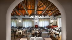 Traditionell eingerichtetes Restaurant mit rustikalem Charme, gemütlichen Holzmöbeln, weiß eingedeckten Tischen und einer offenen Holzbalkendecke – warme Beleuchtung sorgt für ein einladendes Ambiente.