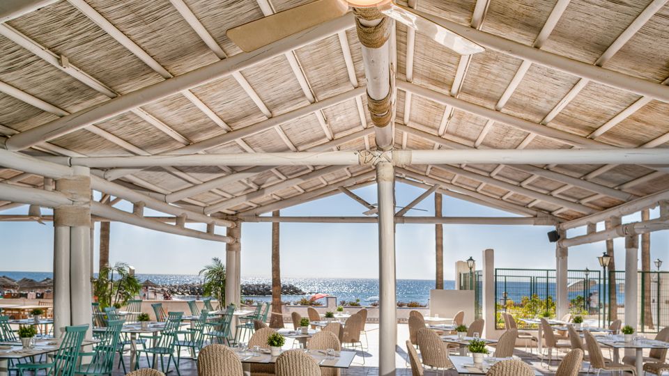 Luftiges Restaurant mit Strohdach und gemütlichen Sitzbereichen, direkt am Meer gelegen – ideal für ein entspanntes Essen mit Meerblick.