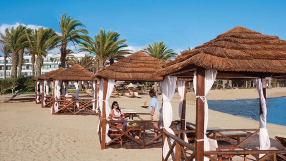 Strohgedeckte Pavillons mit weißen Vorhängen direkt am Sandstrand, umgeben von Palmen.