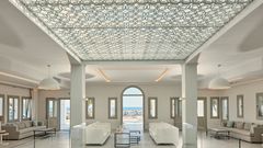 Elegante Hotel-Lobby mit kunstvoller Decke, modernen Sitzgruppen und direktem Blick auf das funkelnde Meer – stilvoller Empfang in traumhafter Umgebung.