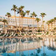 Großzügiger Poolbereich mit Liegen unter Palmen – ideal zum Entspannen und Genießen der Sonne direkt vor dem eleganten Hotelgebäude.