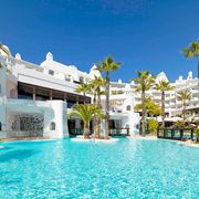 Weitläufige Poollandschaft eines weißen Luxusresorts mit Palmen, Wasserfällen und türkisblauem Wasser – perfekte Kulisse für einen entspannten Urlaub in der Sonne.