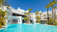 Weitläufige Poollandschaft eines weißen Luxusresorts mit Palmen, Wasserfällen und türkisblauem Wasser – perfekte Kulisse für einen entspannten Urlaub in der Sonne.