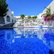 Großer Außenpool eines mediterranen Hotels mit Sonnenliegen, weißen Gebäuden, Palmen und blühender Bougainvillea – perfekte Kulisse für entspannte Urlaubsmomente.