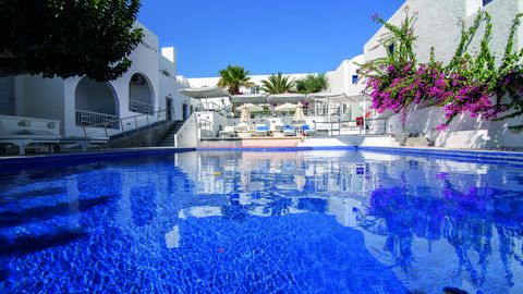 Großer Außenpool eines mediterranen Hotels mit Sonnenliegen, weißen Gebäuden, Palmen und blühender Bougainvillea – perfekte Kulisse für entspannte Urlaubsmomente.