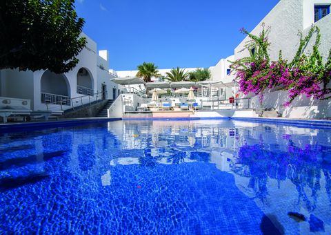 Großer Außenpool eines mediterranen Hotels mit Sonnenliegen, weißen Gebäuden, Palmen und blühender Bougainvillea – perfekte Kulisse für entspannte Urlaubsmomente.