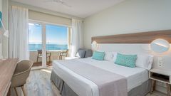 Helles, modern eingerichtetes Hotelzimmer mit Doppelbett, Schreibtisch und Zugang zu einem Balkon mit traumhaftem Meerblick.