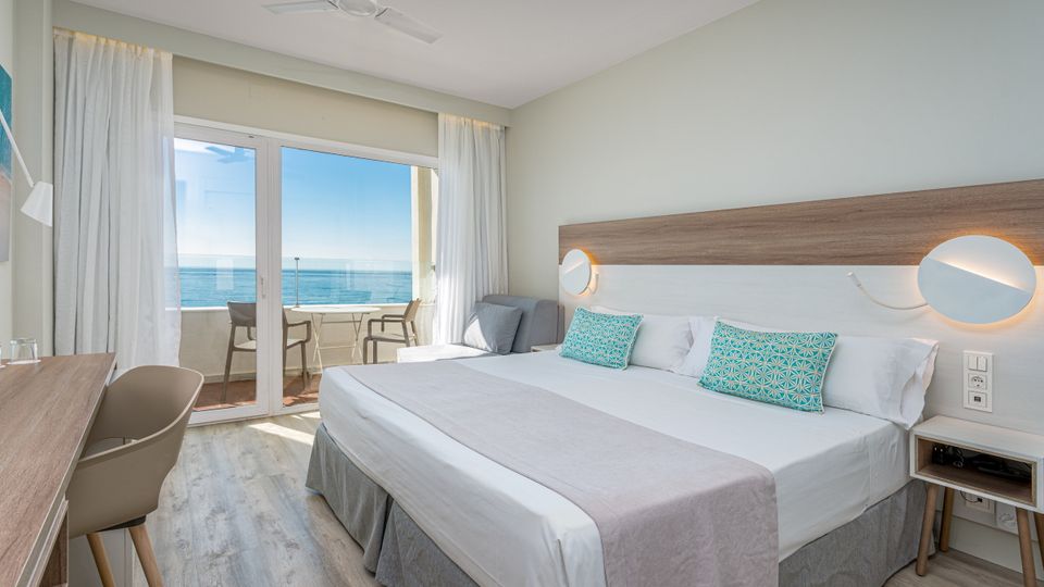 Helles, modern eingerichtetes Hotelzimmer mit Doppelbett, Schreibtisch und Zugang zu einem Balkon mit traumhaftem Meerblick.