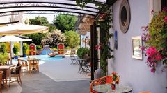 Stilvoll gestalteter Innenhof mit kleinem Brunnen, bunten Wanddekorationen, gemütlichen Sitzplätzen und mediterraner Bepflanzung – lebendige Farben und liebevolle Details sorgen für ein einladendes Ambiente.