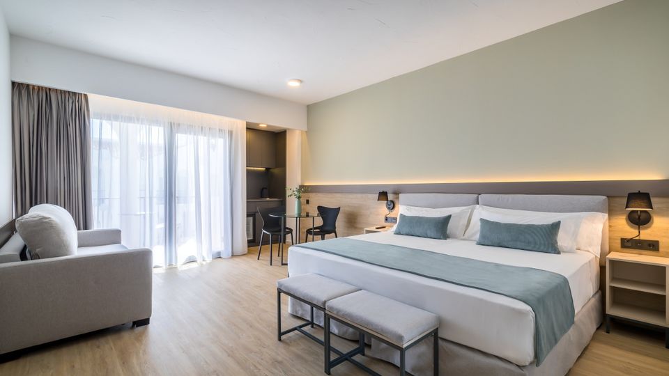 Modernes, geräumiges Hotelzimmer mit Kingsize-Bett, hellen Holzböden, gemütlicher Sitzecke, Schreibtisch und bodentiefen Fenstern, die viel Tageslicht hereinlassen.