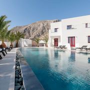 Moderner Poolbereich mit stilvollen Liegen und Palmen, umgeben von weißer Architektur und beeindruckender Bergkulisse – ideal zum Entspannen unter der griechischen Sonne.