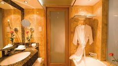 Elegantes Badezimmer in warmen Marmortönen mit großer Spiegelwand, Badewanne, Granitwaschtisch und gemütlichem Bademantel.