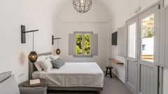 Helles und modern eingerichtetes Doppelzimmer mit schlichter Eleganz, gemütlichem Bett, stylischen Lampen und Blick auf grüne Pinien durch das Fenster.
