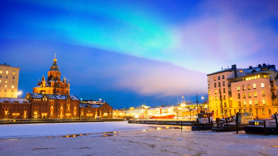 Nordlichter über dem gefrorenen Hafen in Katajanokka mit der orthodoxen Uspenski-Kathedrale in Helsinki