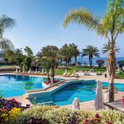 Luxuriöser Pool mit Meerblick, umgeben von Palmen, Blumen und Liegen – perfekte Wohlfühloase.