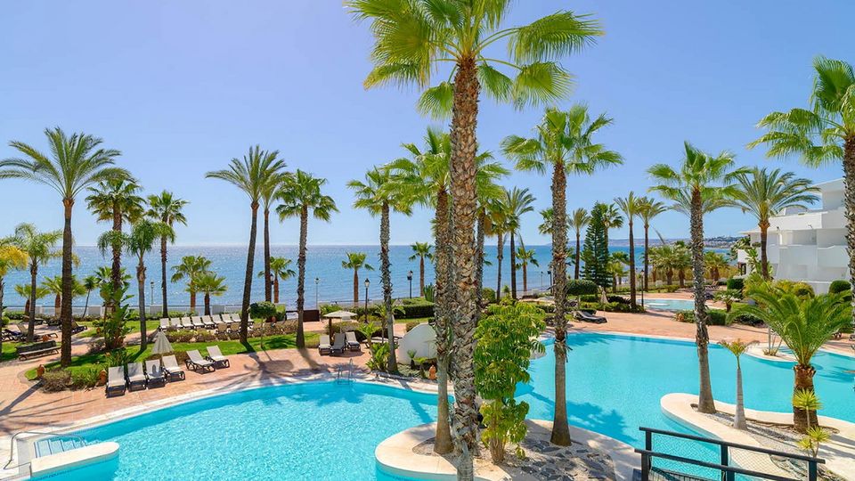 Großzügige Poollandschaft mit Palmen und Meerblick in einer tropischen Hotelanlage bei strahlend blauem Himmel.