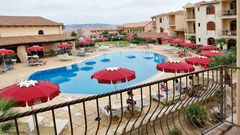 Charmante Hotelanlage im mediterranen Stil mit großem Außenpool, umgeben von Sonnenliegen und roten Sonnenschirmen – ideal für entspannte Urlaubstage.
