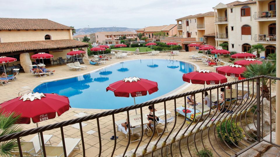 Charmante Hotelanlage im mediterranen Stil mit großem Außenpool, umgeben von Sonnenliegen und roten Sonnenschirmen – ideal für entspannte Urlaubstage.