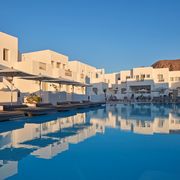 Modernes Hotel im kubischen Stil mit weiß getünchten Fassaden, großzügigem Poolbereich und bequemen Liegen unter Sonnenschirmen – ideal zum Entspannen in der Abendsonne.