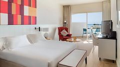 Modern eingerichtetes Hotelzimmer mit großem Doppelbett, stilvollem Sessel, Flachbild-TV und Zugang zu einem möblierten Balkon mit Meerblick.