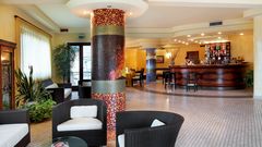 Heller Hotel-Loungebereich mit gemütlichen Sitzgruppen, stilvoller Mosaiksäule und eleganter Bar mit großer Getränkeauswahl – freundliches Ambiente mit modernen und klassischen Elementen.