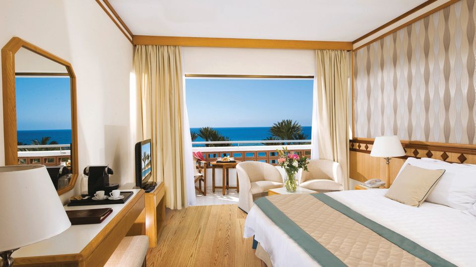 Helles, freundlich eingerichtetes Zimmer mit Meerblick, gemütlicher Sitzecke und Balkon mit Sitzmöbeln.