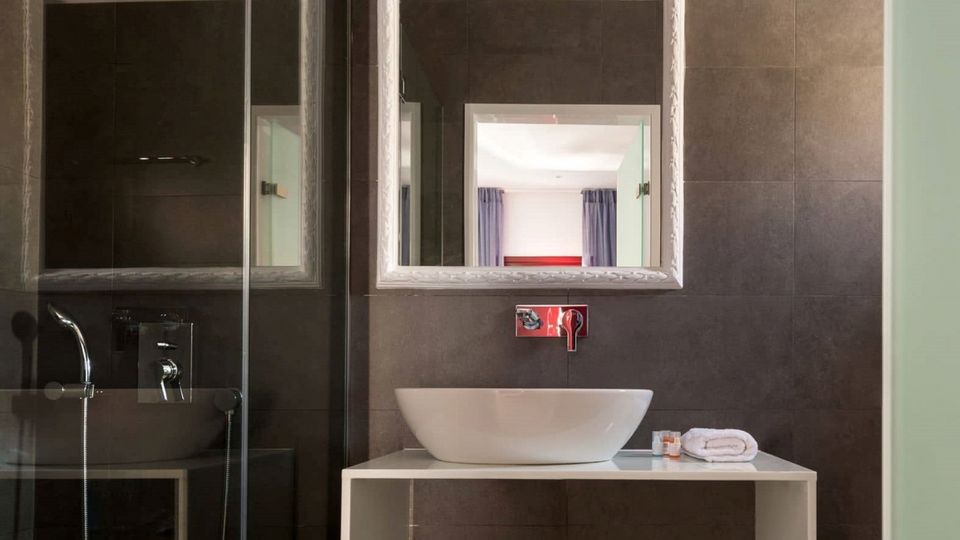 Modernes Badezimmer mit edlen dunklen Fliesen, stilvollem weißen Waschbecken auf einem minimalistischen Waschtisch und beleuchtetem Spiegel – ein eleganter Ort zum Frischmachen.