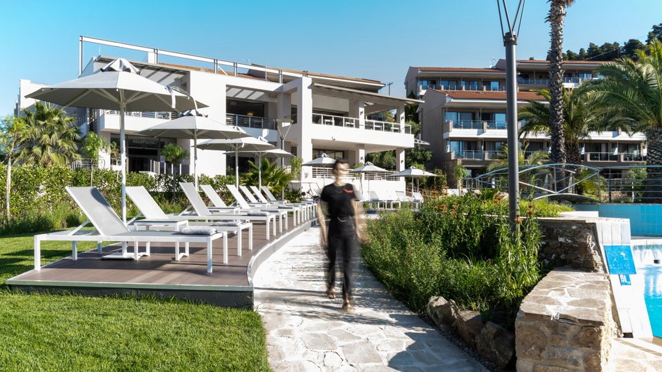 Moderne Hotelanlage mit stilvoller Architektur, großzügigem Poolbereich und komfortablen Sonnenliegen – umgeben von Palmen, Grünflächen und mediterranem Flair.
