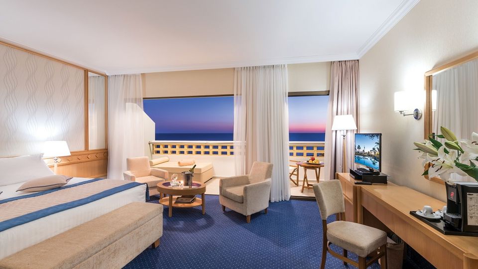 Helles, komfortables Doppelzimmer mit Sitzbereich, Balkon und traumhaftem Meerblick bei Sonnenuntergang.