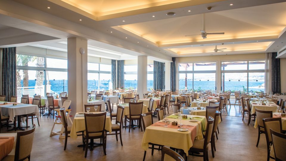 Helles Restaurant mit Meerblick, großen Panoramafenstern und freundlich gedeckten Tischen.
