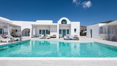 Boutique-Hotel im kykladischen Stil mit strahlend weißer Architektur, türkisfarbenen Fensterläden und großzügigem Poolbereich – stilvolles Design in ruhiger Lage unter klarem, blauem Himmel.