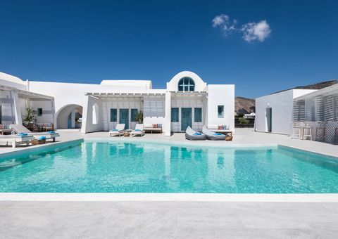 Boutique-Hotel im kykladischen Stil mit strahlend weißer Architektur, türkisfarbenen Fensterläden und großzügigem Poolbereich – stilvolles Design in ruhiger Lage unter klarem, blauem Himmel.