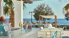 Stilvolle Outdoor-Bar mit erfrischenden Cocktails, weißen Sitzmöbeln und direktem Blick aufs Meer – perfekt für einen entspannten Nachmittag unter Palmen.